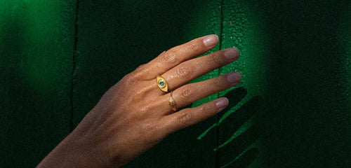 A posed hand dripped in gold rings photographed in front of an emerald green wall Rachel Entwistle