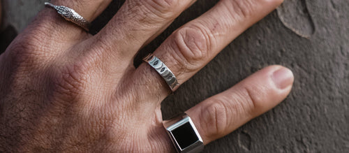 Photograph is zoomed in on a mans hand with three silver rings. The ouroboros ring, Moon phases ring, and Plato ring with a black onyx stone Rachel Entwistle